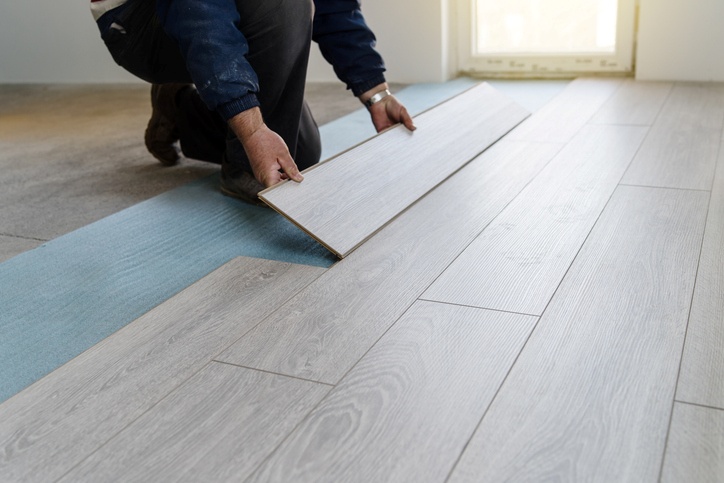 A carpenter lays down new floor panels during home renovations with the sun shining through the door.