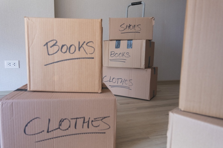 Labeled moving boxes stacked in a room, marked for books, clothes, and shoes.