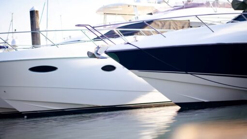 Two boats docked side by side at a marina, showing clean hulls and calm water under clear daylight conditions.