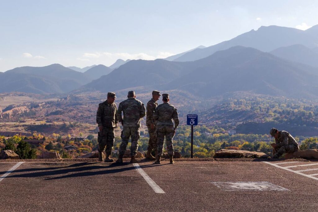 A group of military personnel stands together in front of a beautiful mountain view in Colorado Springs.