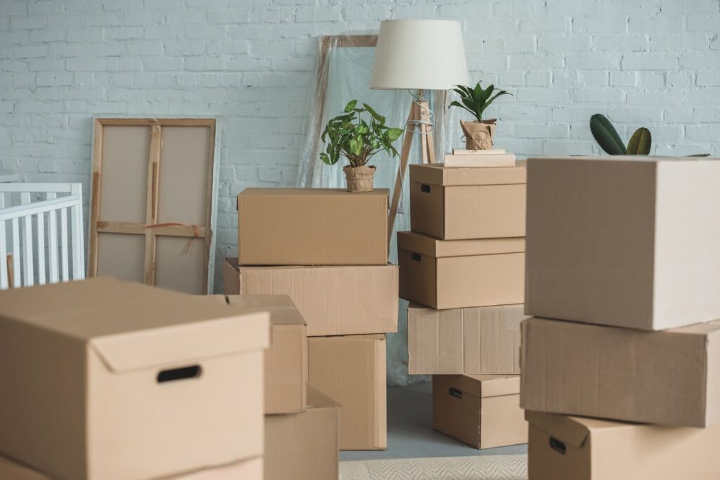 Several cardboard boxes stacked together in a room with a floor lamp and potted plants.